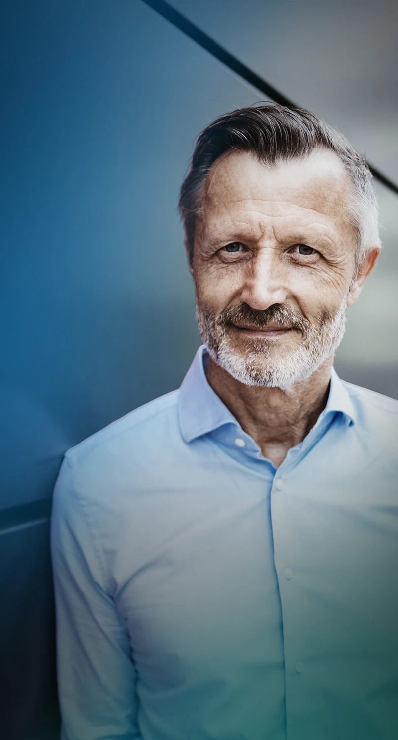 Mann lehnt an einer Wand und lächelt für Imagekampagne in die Kamera